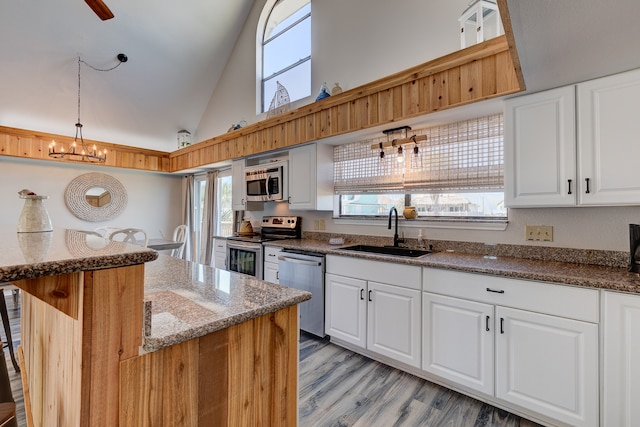 kitchen featuring dark stone countertops, decorative light fixtures, stainless steel appliances, white cabinetry, and a sink