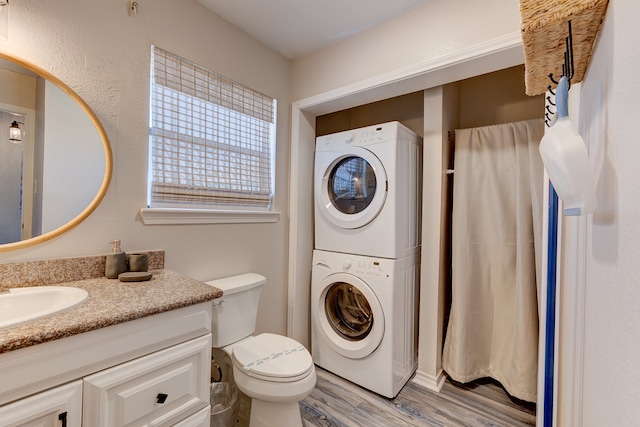 bathroom with hardwood / wood-style flooring, stacked washer and dryer, vanity, and toilet