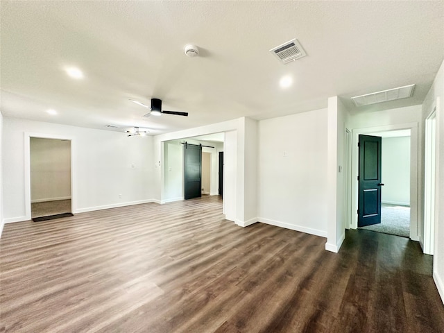 unfurnished room featuring ceiling fan, a barn door, dark hardwood / wood-style flooring, and a textured ceiling