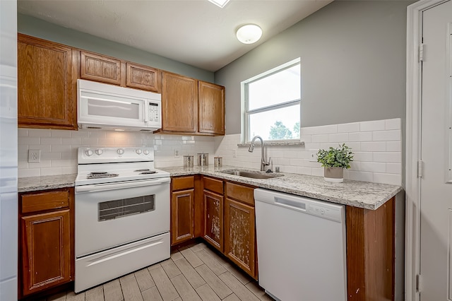 kitchen with decorative backsplash, white appliances, light stone countertops, and sink