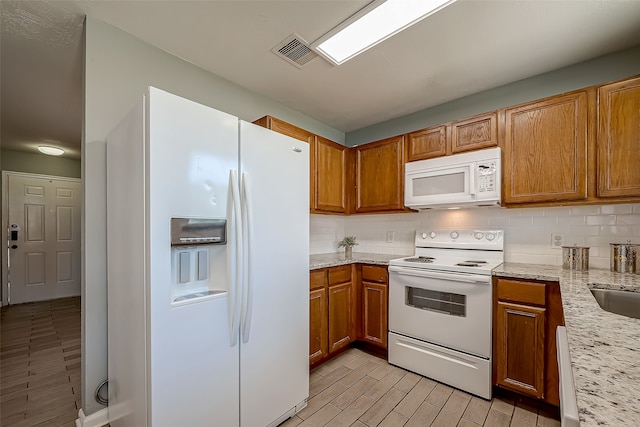 kitchen with light stone countertops, backsplash, and white appliances