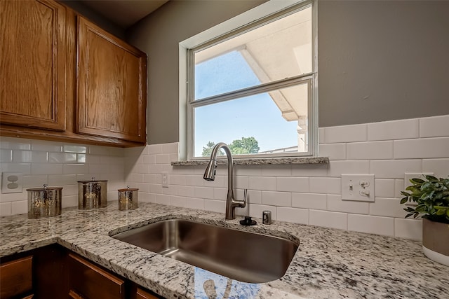 kitchen with backsplash, light stone counters, plenty of natural light, and sink