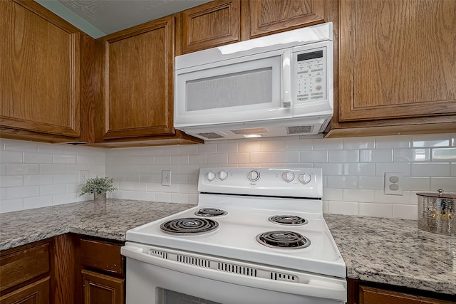 kitchen featuring decorative backsplash, white appliances, and light stone counters