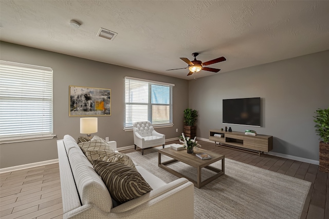 living room with ceiling fan, a textured ceiling, and light hardwood / wood-style flooring