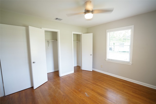 unfurnished bedroom with ceiling fan, multiple closets, and hardwood / wood-style flooring