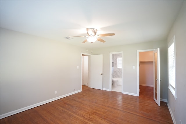 unfurnished bedroom with ensuite bathroom, ceiling fan, hardwood / wood-style floors, and a walk in closet