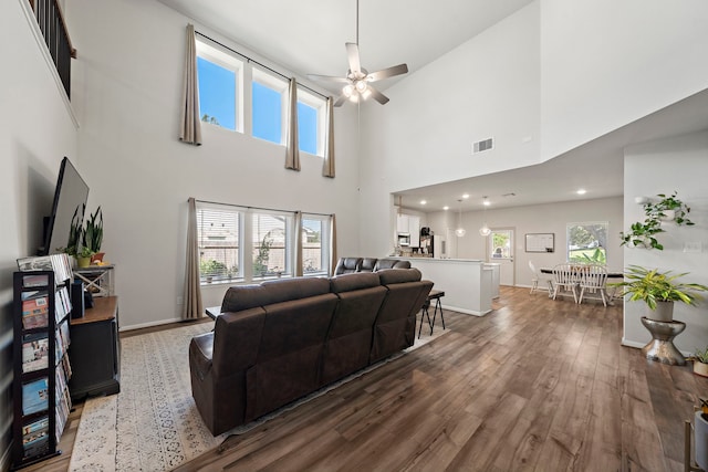 living room with a towering ceiling, ceiling fan, and dark hardwood / wood-style flooring