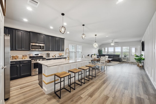 kitchen featuring a kitchen bar, light hardwood / wood-style floors, stainless steel appliances, decorative light fixtures, and a center island with sink