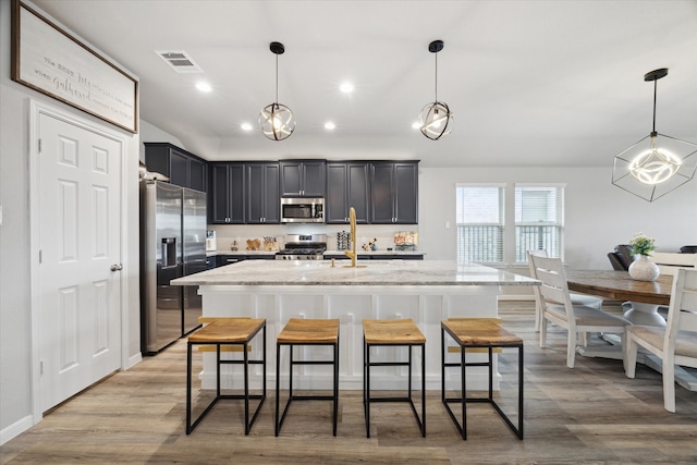 kitchen featuring appliances with stainless steel finishes, a kitchen island with sink, hanging light fixtures, and light wood-type flooring