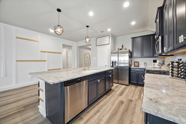 kitchen featuring appliances with stainless steel finishes, light hardwood / wood-style flooring, hanging light fixtures, and a center island with sink