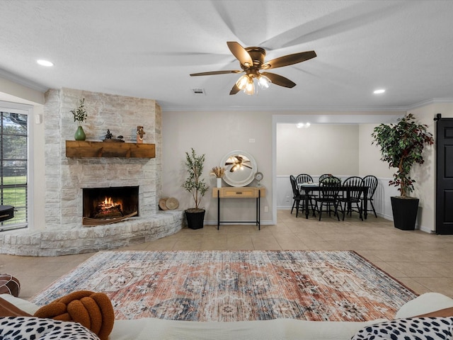 living room featuring ceiling fan, a stone fireplace, light tile patterned floors, and crown molding