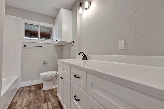 bathroom with a bath, vanity, hardwood / wood-style floors, and toilet