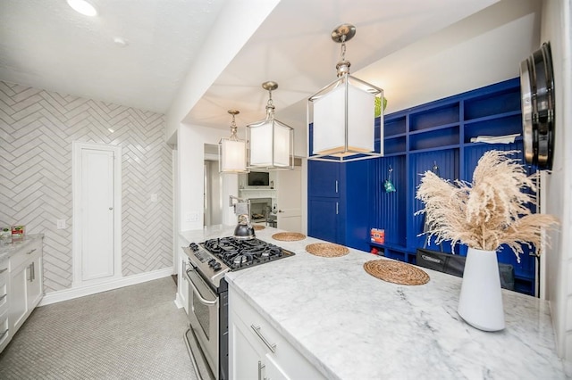 kitchen with stainless steel gas stove, white cabinetry, light stone counters, and decorative light fixtures