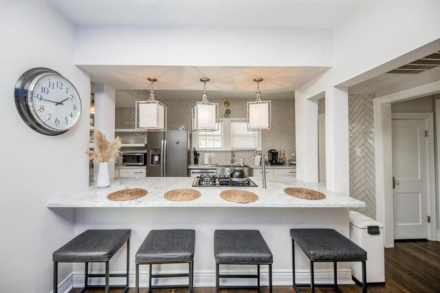 kitchen featuring dark hardwood / wood-style flooring, stainless steel appliances, pendant lighting, and a breakfast bar area