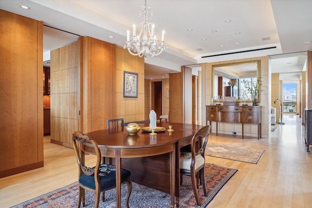 dining room with a notable chandelier, wooden walls, and light hardwood / wood-style floors