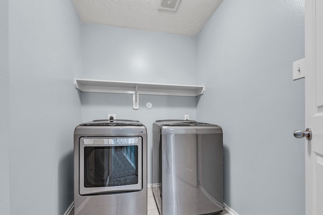 clothes washing area featuring a textured ceiling, independent washer and dryer, and light tile patterned flooring