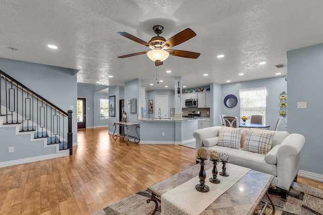 living room featuring a textured ceiling, ceiling fan, light hardwood / wood-style flooring, and sink