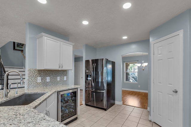 kitchen with light tile patterned flooring, sink, beverage cooler, stainless steel refrigerator with ice dispenser, and white cabinets