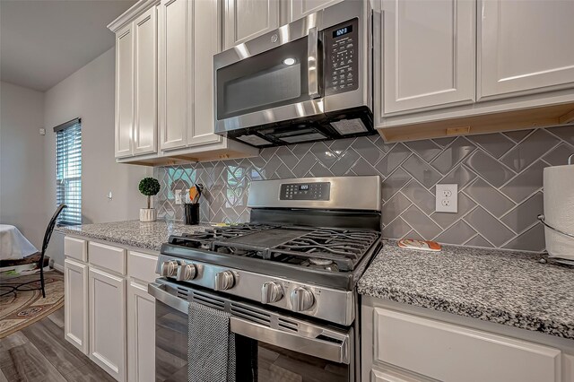 kitchen with light stone counters, white cabinets, stainless steel appliances, and dark hardwood / wood-style floors