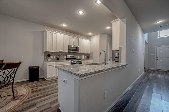 kitchen with white cabinets, kitchen peninsula, light stone countertops, stainless steel appliances, and dark hardwood / wood-style floors