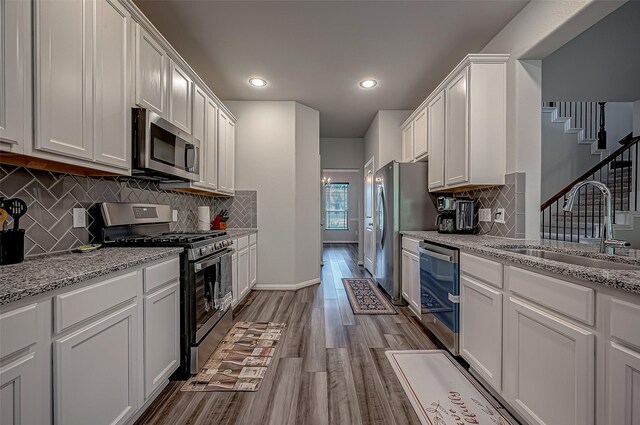 kitchen with white cabinetry, light stone counters, stainless steel appliances, light wood-type flooring, and sink