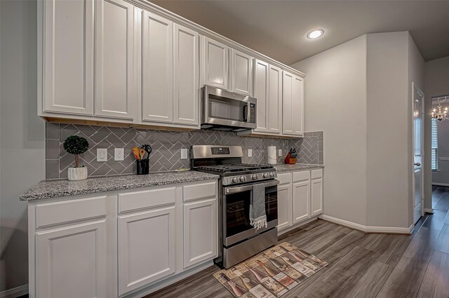 kitchen with appliances with stainless steel finishes, white cabinetry, backsplash, light stone countertops, and wood-type flooring