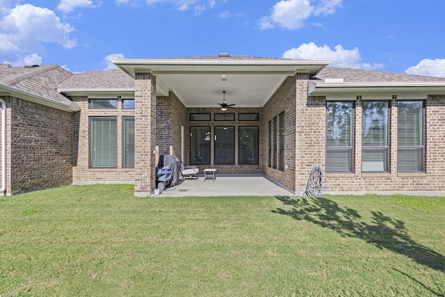 rear view of house with ceiling fan, a patio, brick siding, and a lawn