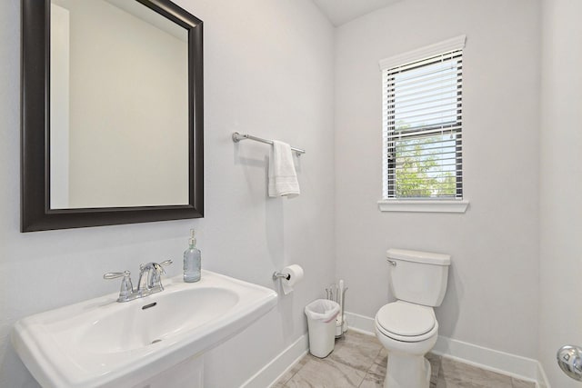 half bathroom with toilet, a sink, marble finish floor, and baseboards