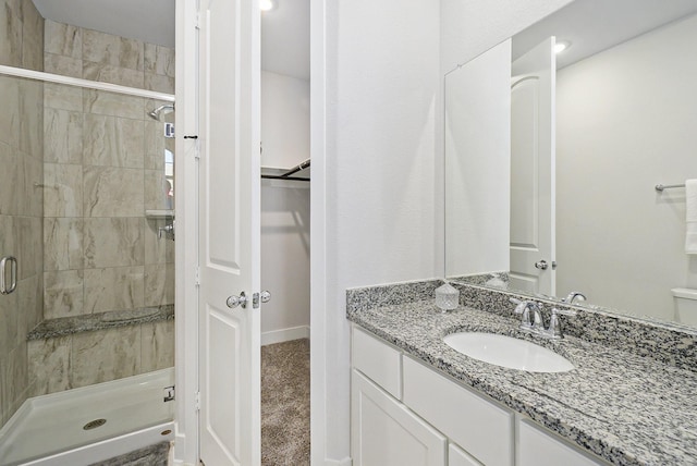 full bathroom with a stall shower, a walk in closet, vanity, and baseboards