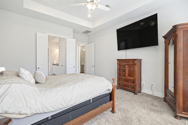 bedroom with a raised ceiling, visible vents, ensuite bathroom, light carpet, and baseboards