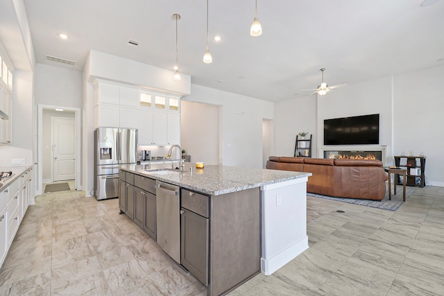 kitchen featuring sink, white cabinets, appliances with stainless steel finishes, decorative light fixtures, and light stone countertops