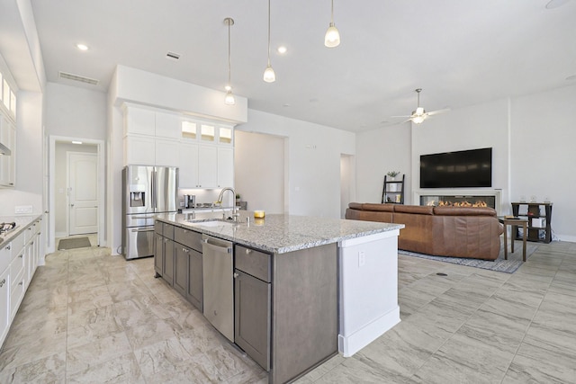 kitchen featuring glass insert cabinets, appliances with stainless steel finishes, light stone counters, white cabinetry, and a sink