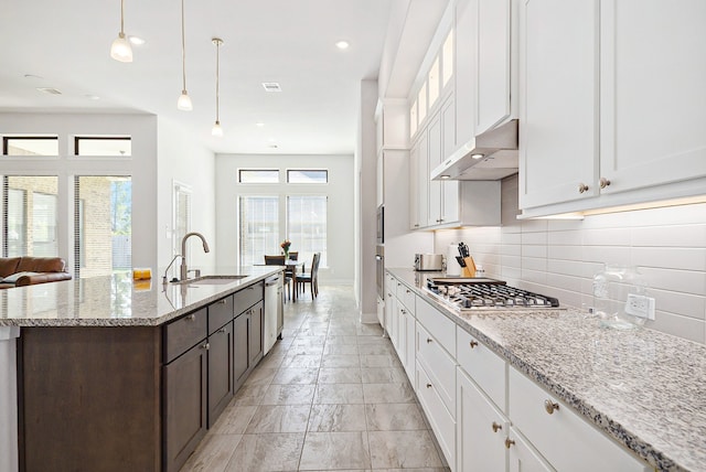 kitchen with sink, white cabinets, hanging light fixtures, appliances with stainless steel finishes, and light stone countertops