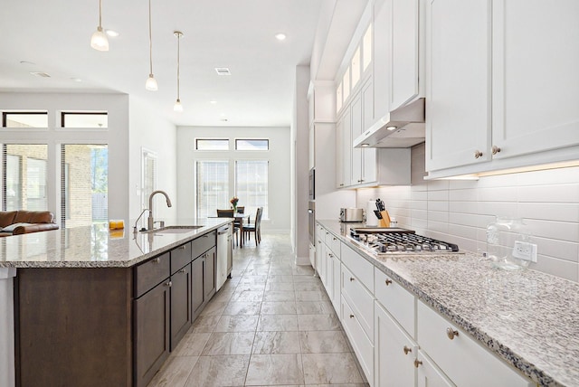 kitchen featuring hanging light fixtures, stainless steel appliances, under cabinet range hood, white cabinetry, and a sink