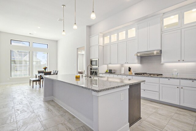 kitchen featuring hanging light fixtures, a center island with sink, and white cabinetry