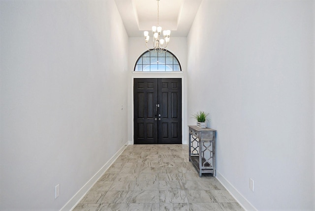 foyer entrance featuring a chandelier, marble finish floor, a raised ceiling, and baseboards