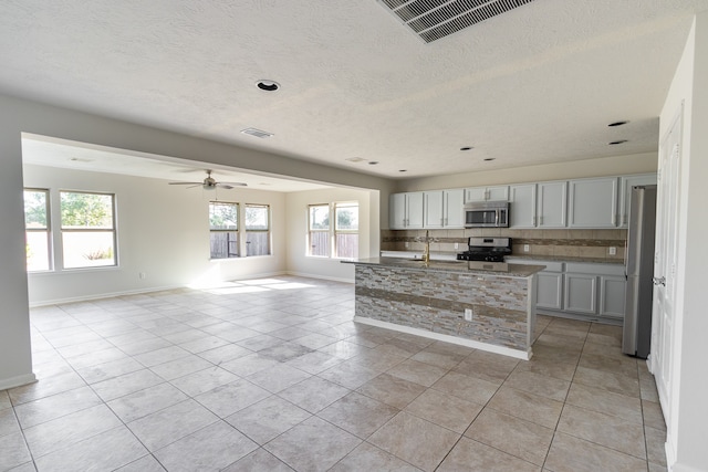 kitchen featuring decorative backsplash, gray cabinetry, light tile patterned flooring, an island with sink, and stainless steel appliances