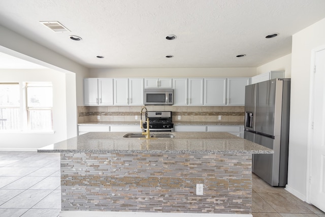 kitchen featuring light stone counters, white cabinets, sink, a kitchen island with sink, and stainless steel appliances