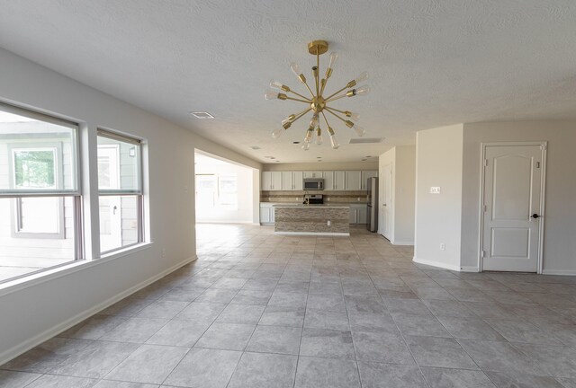 unfurnished living room with a textured ceiling, light tile patterned floors, and a notable chandelier