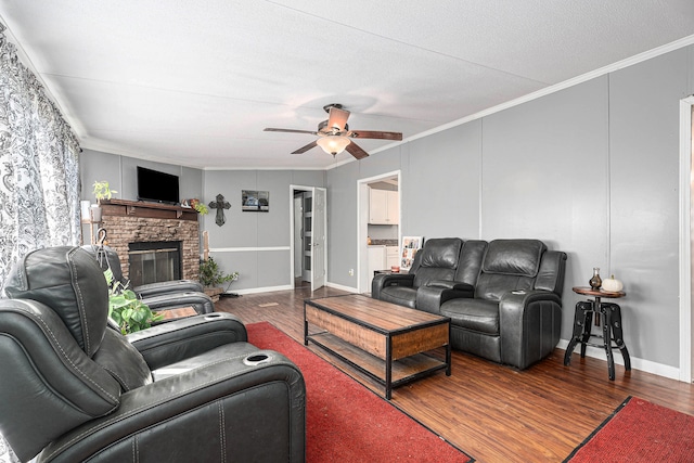 living room featuring dark wood-type flooring, a brick fireplace, ceiling fan, ornamental molding, and a textured ceiling