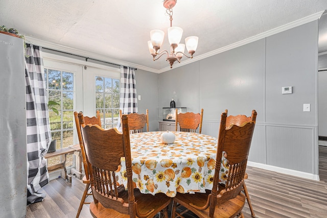 dining space with hardwood / wood-style floors, a textured ceiling, crown molding, and an inviting chandelier