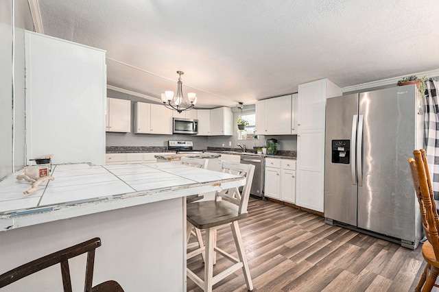 kitchen with a kitchen bar, appliances with stainless steel finishes, dark hardwood / wood-style flooring, pendant lighting, and white cabinets