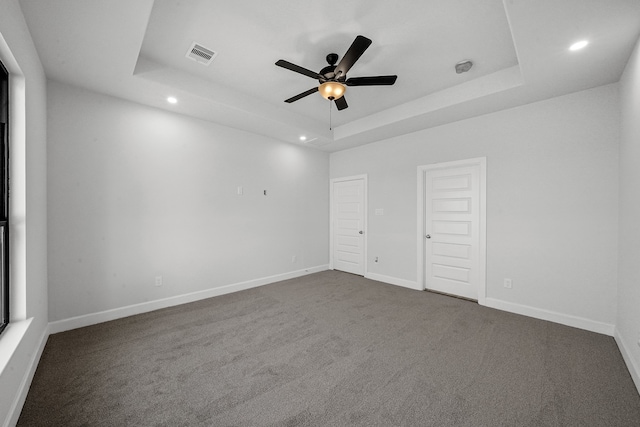 unfurnished bedroom featuring dark colored carpet, ceiling fan, and a raised ceiling