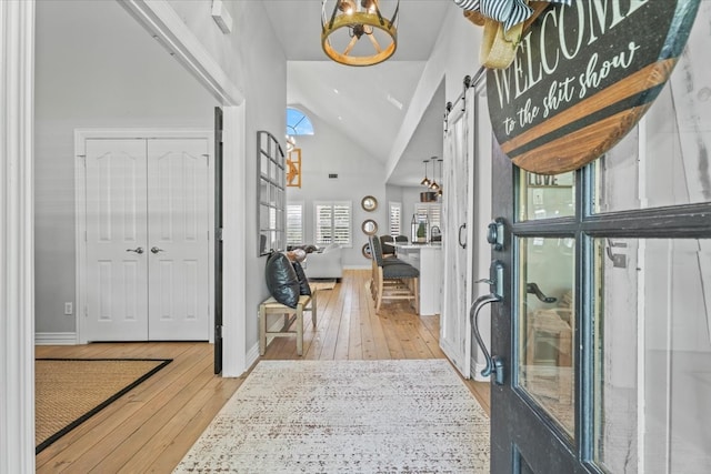 entrance foyer with high vaulted ceiling, a barn door, hardwood / wood-style floors, and a chandelier