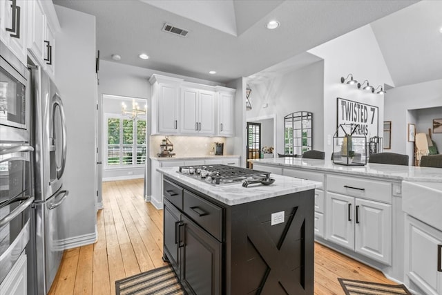 kitchen with appliances with stainless steel finishes, white cabinetry, a center island, and light hardwood / wood-style flooring