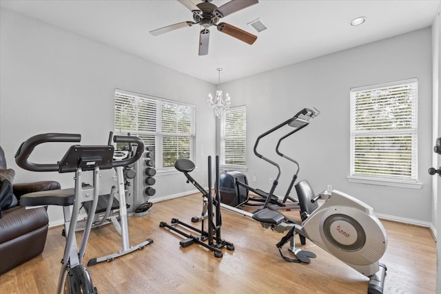 workout area with ceiling fan with notable chandelier, light wood-type flooring, and a wealth of natural light