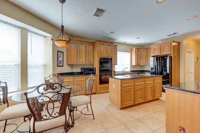 kitchen with a center island, dark stone counters, black appliances, decorative light fixtures, and light tile patterned flooring