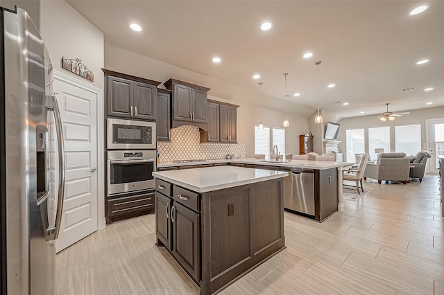 kitchen with kitchen peninsula, stainless steel appliances, dark brown cabinets, decorative light fixtures, and sink