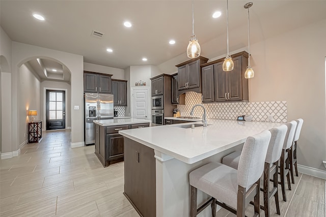 kitchen featuring pendant lighting, sink, kitchen peninsula, backsplash, and stainless steel appliances