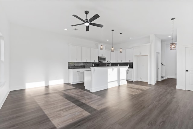 kitchen with an island with sink, hanging light fixtures, sink, dark wood-type flooring, and white cabinetry